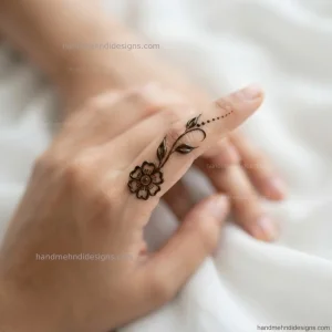 Finger floral mehndi featuring a small flower at the base of the middle finger with a thin leafy stem and tiny dots.