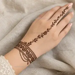 Bracelet-style back hand mehndi featuring a tiny floral wrist band, dotted edging, and a fine diagonal chain extending toward the index finger.