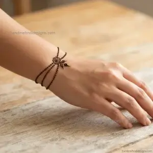 Back hand mehndi showing two fine dotted wrist chains joined by a tiny flower and small leaves.