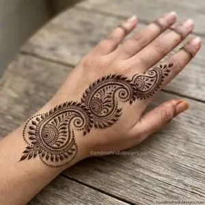 Back hand diagonal paisley mehndi design featuring three curved paisley motifs, fine inner curls, leaf borders, and tiny decorative dots.